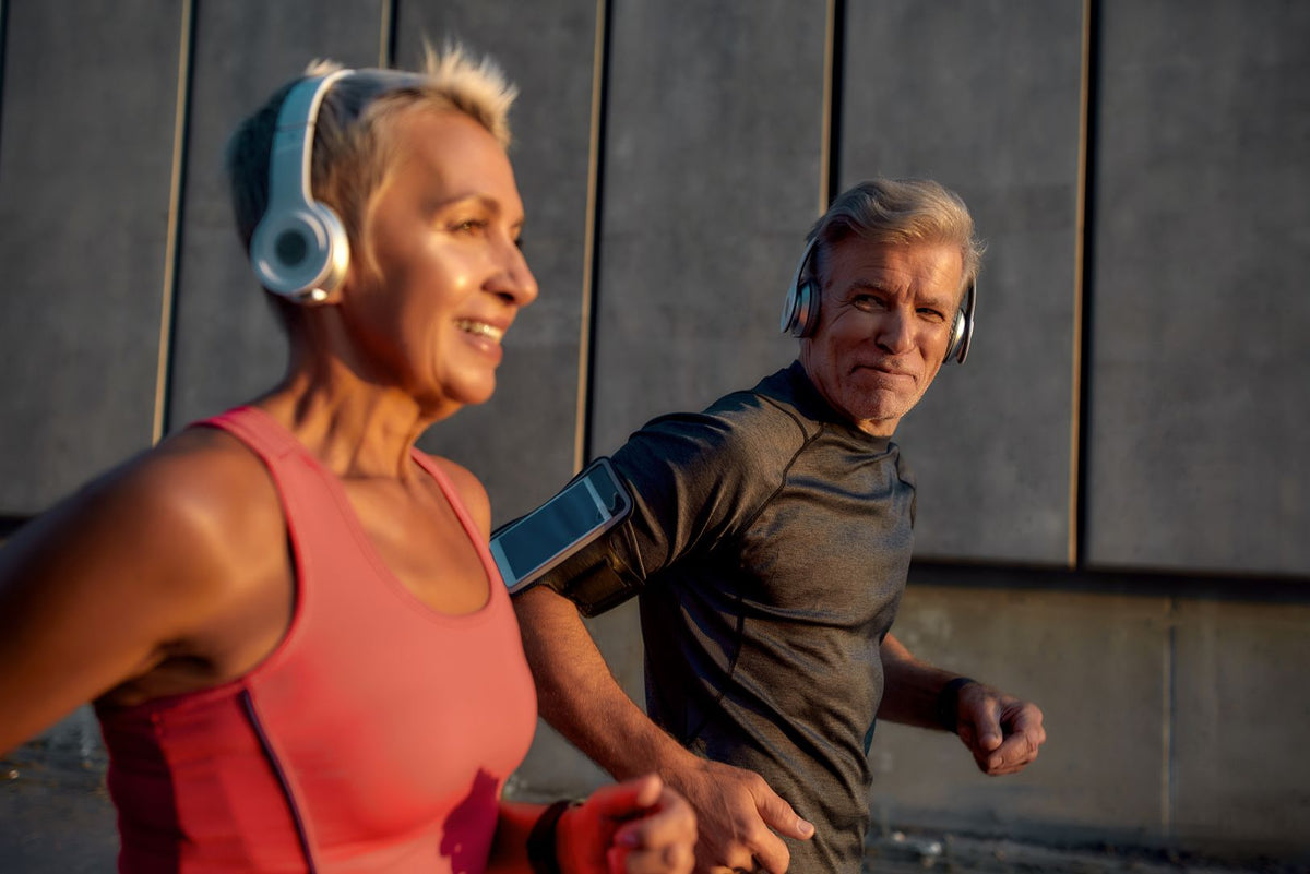 Two people exercising outdoors with headphones on a gray wall background