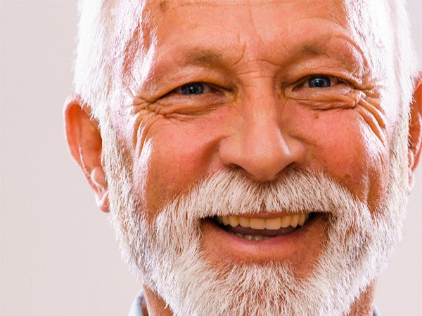 Close-up of a smiling man with a white beard against a light background