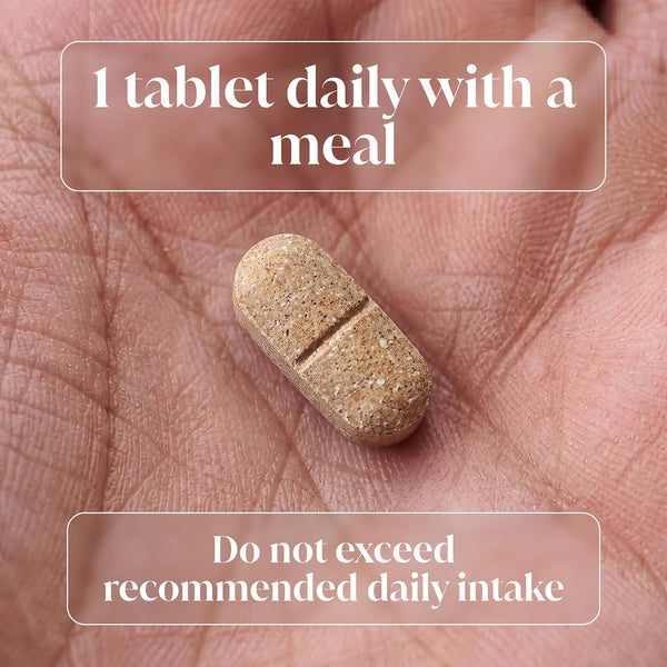 A single beige oval tablet with a scored line down the center rests on an open palm. White text overlays read '1 tablet daily with a meal' and 'Do not exceed recommended daily intake'.