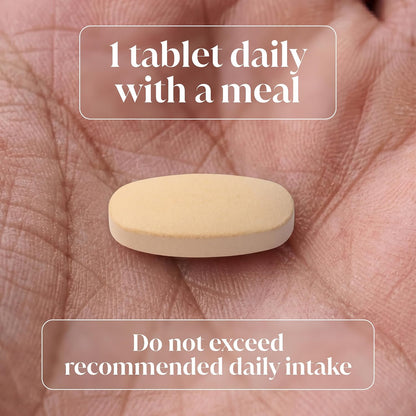 A single beige oval tablet resting on an open palm, with text overlays reading '1 tablet daily with a meal' and 'Do not exceed recommended daily intake'.