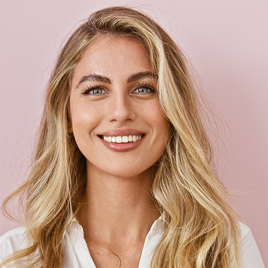 Woman with blonde hair and blue eyes smiling against a pink background