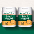 Two white plastic supplement bottles of Nature's Best Rutin & Vitamin C 500mg, each containing 90 tablets, displayed side-by-side on a dark green surface against a textured off-white background.