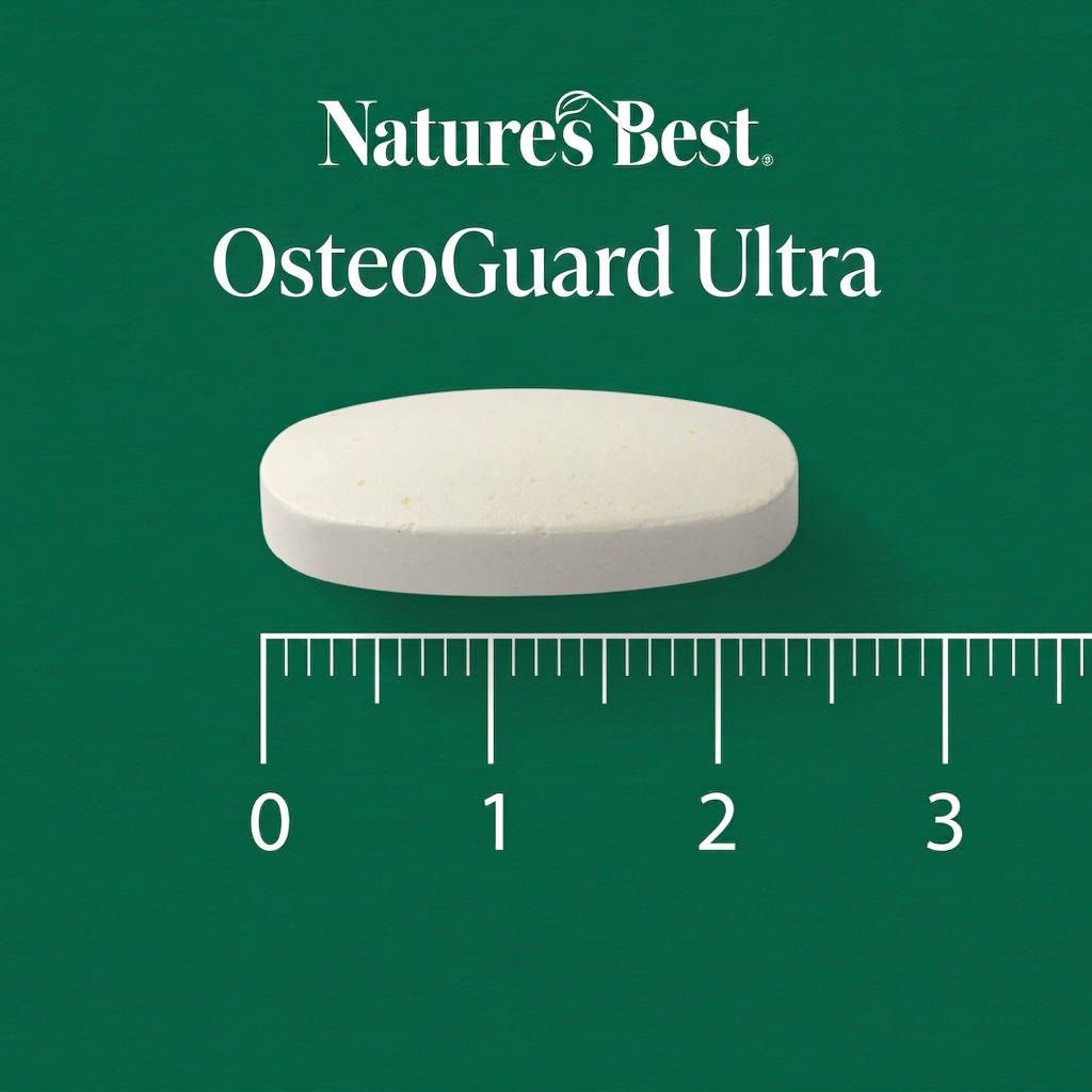 A single white oval tablet labeled Natures Best OsteoGuard Ultra is shown on a dark green background with a ruler underneath for scale.
