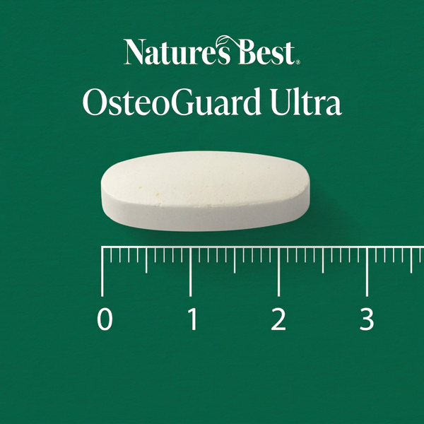 A single white oval tablet labeled Natures Best OsteoGuard Ultra is shown on a dark green background with a ruler underneath for scale.