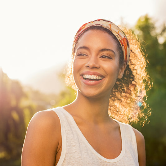 Woman with a headband smiling outdoors with a blurred natural background