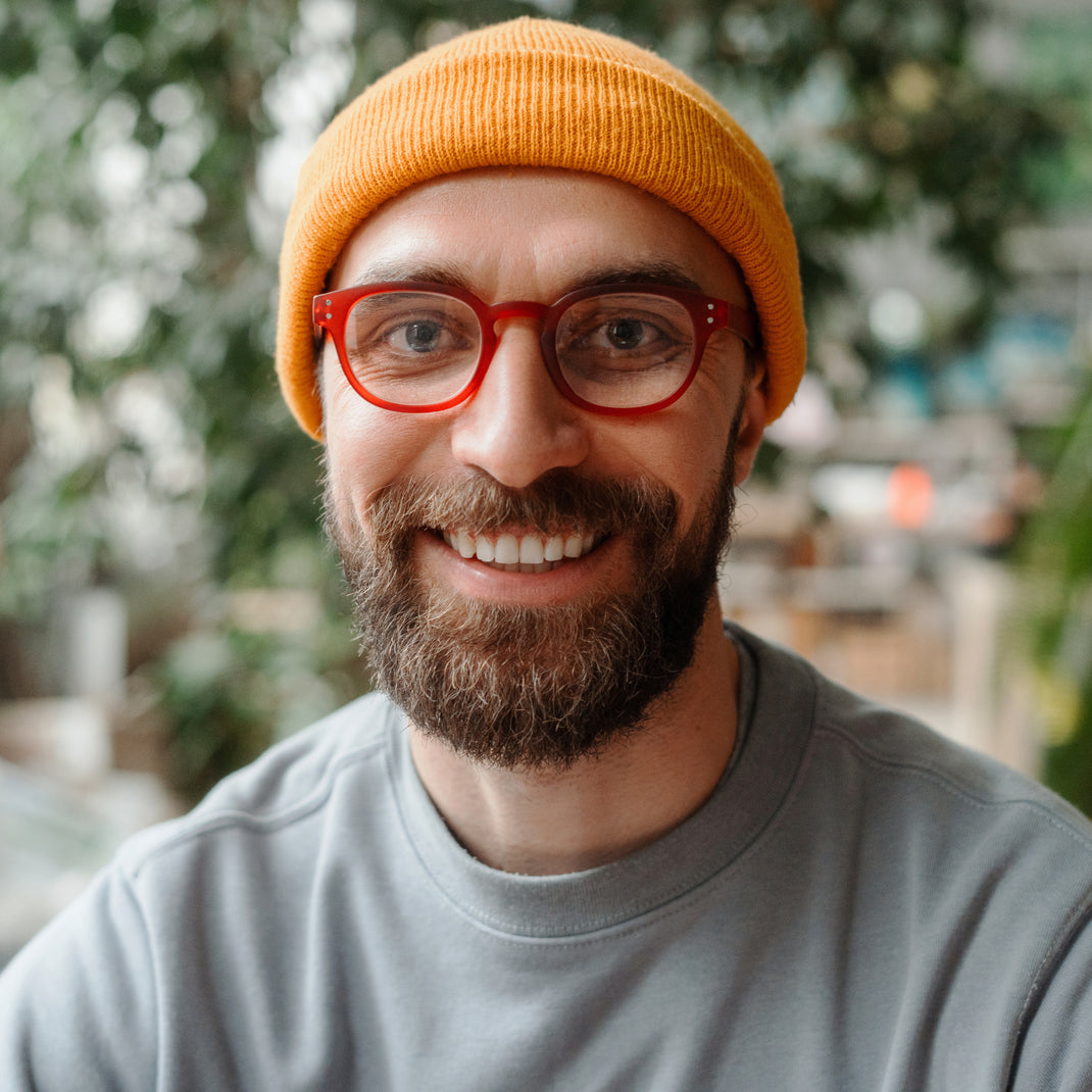 Man wearing a yellow beanie and red glasses with a blurred outdoor background