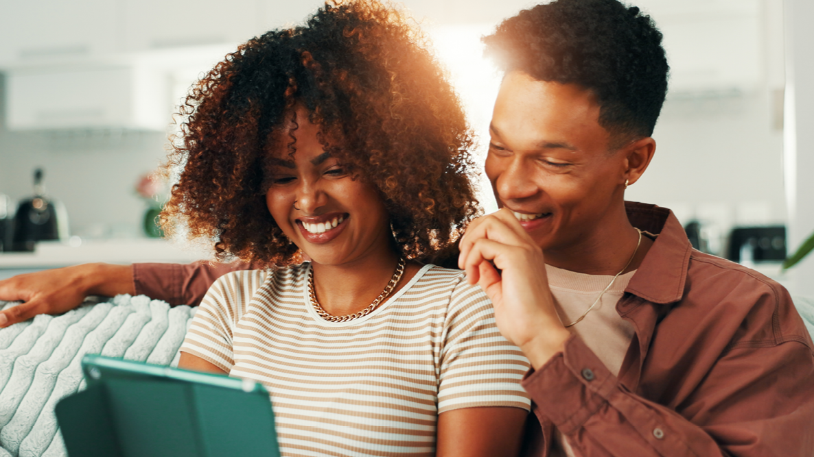 Two people smiling and looking at a tablet together in an office setting.