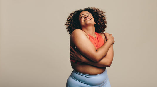 Woman in an orange top and blue pants against a beige background